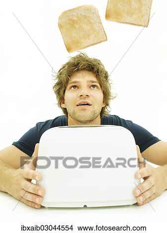 Young man looking at slices of toast as they pop out of a toaster View Large Photo Image Picture - Young man looking at slices of toast as they pop out of a toaster. Fotosearch