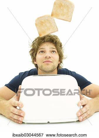 Stock Photo - Young man looking at slices of toast as they pop out of a toaster. Fotosearch