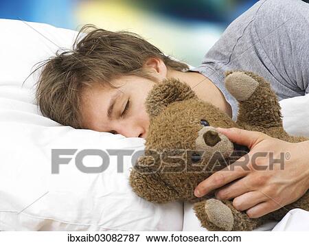 Young man lying asleep in bed with a teddy bear View Large Photo Image Stock Photo - Young man lying asleep in bed with a teddy bear. Fotosearch