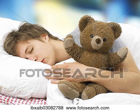 Stock Photo - Young man lying asleep in bed with a teddy bear. Fotosearch
