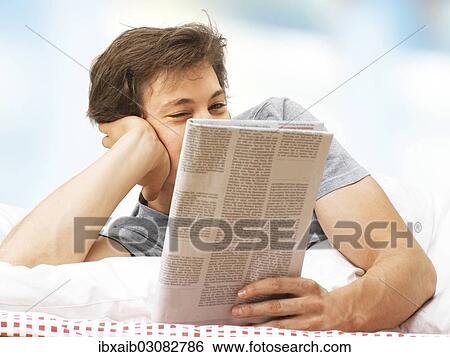 "Young man lying in bed, reading a newspaper" View Large Photo Image Stock Photograph - "Young man lying in bed, reading a newspaper". Fotosearch
