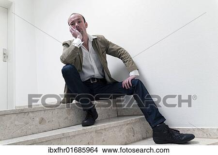 Picture - Young man sitting alone on the stairs in a hallway. Fotosearch