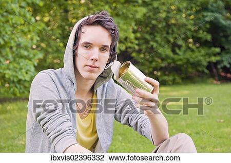 "Young man sitting in nature, holding an old can" View Large Photo Image Stock Image - "Young man sitting in nature, holding an old can". Fotosearch