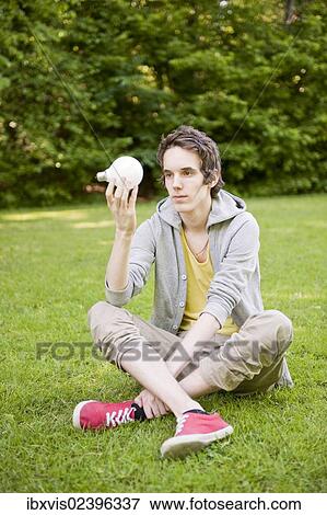"Young man sitting in nature, holding lightbulb" View Large Photo Image Stock Photo - "Young man sitting in nature, holding lightbulb". Fotosearch