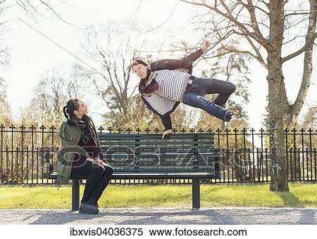 "Young man trying to impress indifferent girl by jumping over a park bench, Sweden, Europe" View Large Photo Image Stock Photography - "Young man trying to impress indifferent girl by jumping over a park bench, Sweden, Europe". Fotosearch