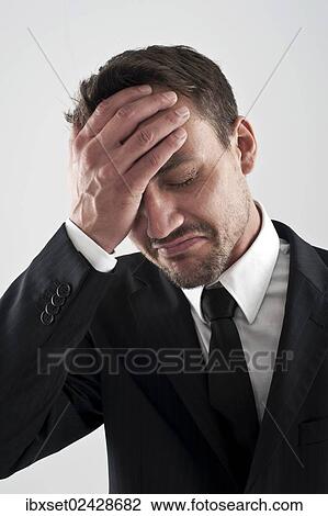 "Young man wearing a suit holding his hand on his forehead, worried" View Large Photo Image Stock Image - "Young man wearing a suit holding his hand on his forehead, worried". Fotosearch
