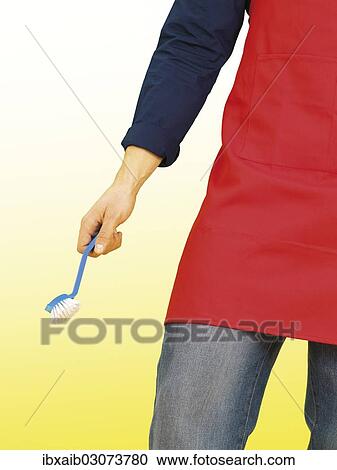 "Young man wearing an apron while doing the housework, holding a scrubbing brush" View Large Photo Image Stock Image - "Young man wearing an apron while doing the housework, holding a scrubbing brush". Fotosearch