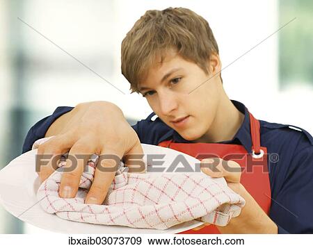 "Young man wearing an apron while doing the housework, drying a plate" View Large Photo Image Stock Photo - "Young man wearing an apron while doing the housework, drying a plate". Fotosearch