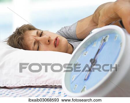 Stock Image - "Young man with an alarm clock, early in the morning, tired, sleepy". Fotosearch