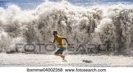 Stock Photo - "Young man with sunglasses running from a high wave, La Palma, Canary Islands, Spain, Europe". Fotosearch