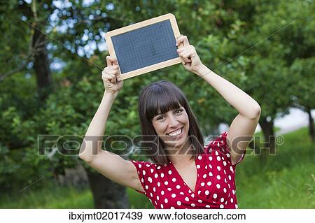 Stock Photo - "Young woman, 25, holding a blackboard in her hands". Fotosearch