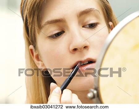 Stock Image - "Young woman applying make-up, lip gloss". Fotosearch