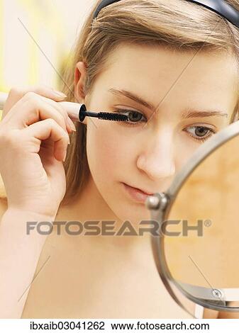 Stock Image - "Young woman applying make-up, mascara". Fotosearch