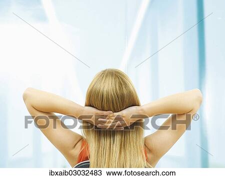 Stock Image - "Young woman, blond, sitting on a chair, relaxing, rear view". Fotosearch