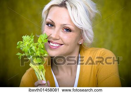 Stock Image - Young woman holding a stick of celery. Fotosearch