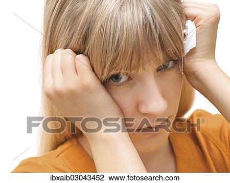Stock Image - "Young woman holding a tissue, angry, sad". Fotosearch