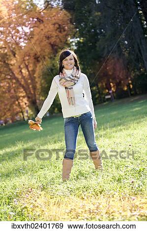 "Young woman holding autumn leaves, standing in autumnal park" View Large Photo Image Stock Photo - "Young woman holding autumn leaves, standing in autumnal park". Fotosearch