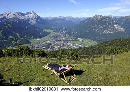 "Young woman in a deck chair, view of Garmisch-Partenkirchen, Zugspitze mountain, Jubilaeumsgrat ridge and Alpspitze mountain as seen from Wank mountain, Upper Bavaria, Bavaria, Germany, Europe" View Large Photo Image Stock Image - "Young woman in a deck chair, view of Garmisch-Partenkirchen, Zugspitze mountain, Jubilaeumsgrat ridge and Alpspitze mountain as seen from Wank mountain, Upper Bavaria, Bavaria, Germany, Europe". Fotosearch