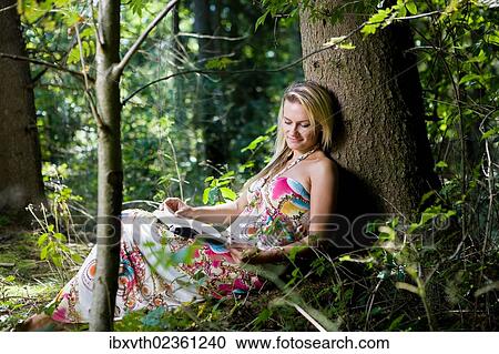Stock Image - "Young woman in the forest, reading". Fotosearch