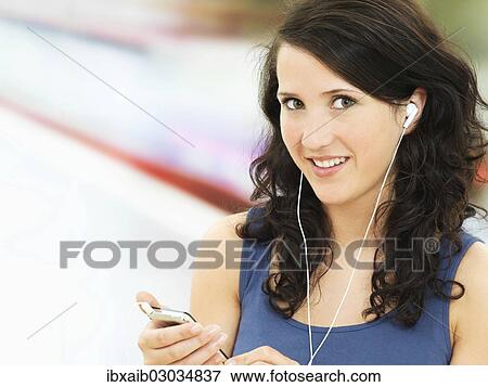 Stock Photo - Young woman listening to music at a subway station. Fotosearch