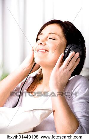Young woman listening to music on headphones in the living room View Large Photo Image Stock Photo - Young woman listening to music on headphones in the living room. Fotosearch