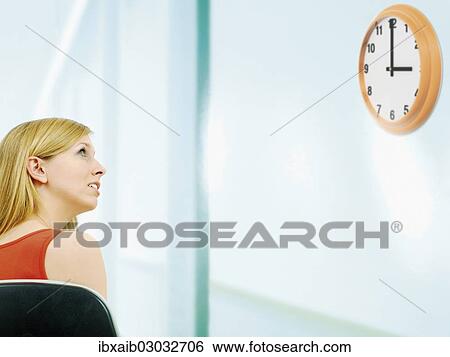 Stock Photograph - Young woman looking at a clock. Fotosearch
