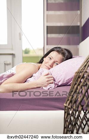 Young woman lying in bed in a bedroom View Large Photo Image Stock Image - Young woman lying in bed in a bedroom. Fotosearch