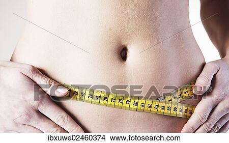 Picture - Young woman measuring her waist with a tape measure. Fotosearch