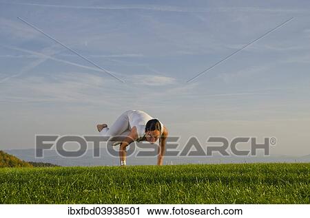 Stock Image - "Young woman practising Hatha yoga, here the pose parshva kakasana, parshva bakasana, sideward crow pose or sideward crane pose". Fotosearch