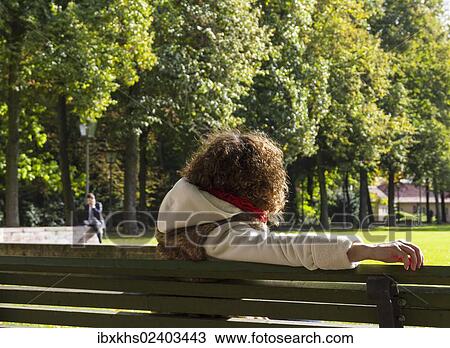 "Young woman sitting on a bench watching a man speaking on the phone, Berlin, Germany, Europe" View Large Photo Image Stock Image - "Young woman sitting on a bench watching a man speaking on the phone, Berlin, Germany, Europe". Fotosearch