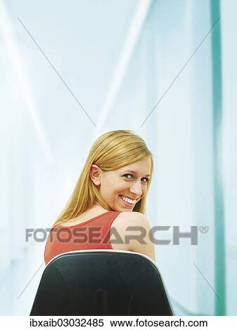"Young woman sitting on chair, turning from a rear view, smiling" View Large Photo Image Stock Photography - "Young woman sitting on chair, turning from a rear view, smiling". Fotosearch