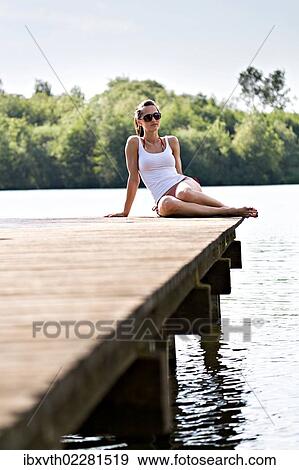 Young woman sitting on jetty at lakeside View Large Photo Image Stock Photo - Young woman sitting on jetty at lakeside. Fotosearch