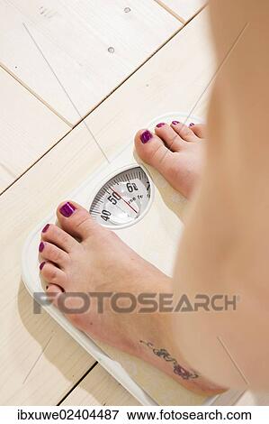 Young Woman Standing On A Scale And Checking Her Weight Stock Photo Ibxuwe Fotosearch