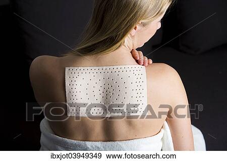 Stock Photo - Young woman suffering from back pain has applied a heat plaster. Fotosearch