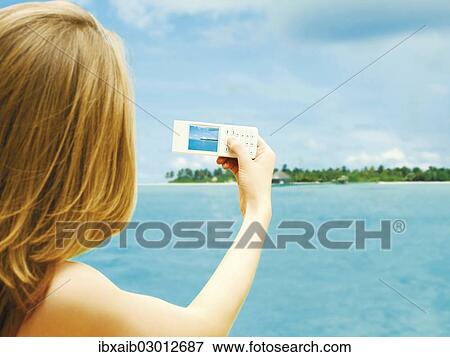 Stock Photo - "Young woman taking a photo with a mobile phone, holiday, Caribbean". Fotosearch