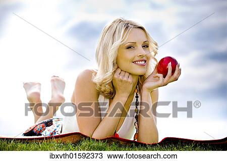 Stock Image - Young woman with apple in a meadow. Fotosearch