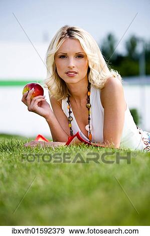 Stock Photo - Young woman with apple in a meadow. Fotosearch