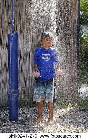 Stock Image - 5-year-old boy wearing a blue t-shirt standing under a running shower in a garden, Vassiliki, Lefkas, Greece, Europe. Fotosearch