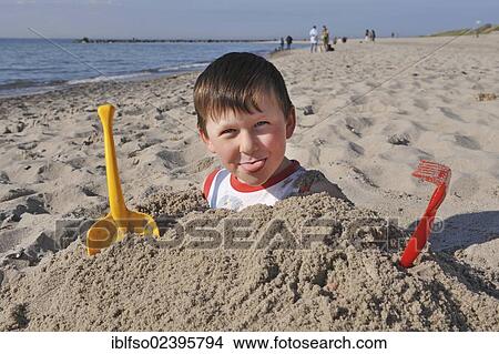 Picture - "6-year-old boy, buried in sand up to his shoulders, beach near Ahrenshoop, Baltic Sea, Mecklenburg-Western Pomerania, Germany, Europe". Fotosearch