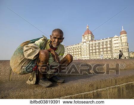 Stock Image - "A beggar is sitting in front of the luxurios Taj Mahal Palace Hotel in the suburb Colaba, Mumbai, Maharashtra, India, Asia". Fotosearch