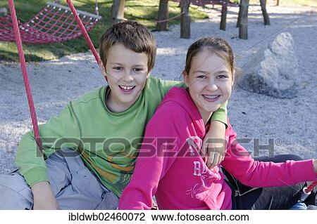 Stock Image - "A boy and girl sitting on a playground, Schliersbergalm alp, near lake Schliersee, Upper Bavaria, Bavaria, Germany, Europe". Fotosearch