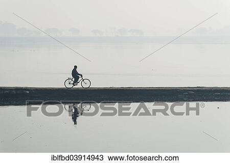 Stock Image - "A cyclist crossing the Yamuna river on a dam in the morning haze, Vrindavan, Uttar Pradesh, India, Asia". Fotosearch