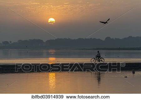 Stock Photo - "A cyclist crossing the Yamuna river on a dam at sunrise, Vrindavan, Uttar Pradesh, India, Asia". Fotosearch
