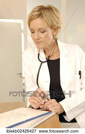 A female doctor in a white coat with stethoscope is standing at a reception desk View Large Photo Image Stock Photo - A female doctor in a white coat with stethoscope is standing at a reception desk. Fotosearch