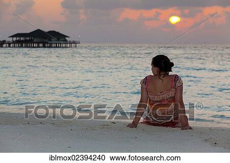 Stock Image - "A girl, about 15 years old, sitting on the beach watching the sunset, North Male Atoll, Republic of Maldives, Indian Ocean, Asia". Fotosearch