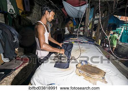 Stock Image - "A labourer is ironing laundry at Mahalaxmi Dhobi Ghat, laundry district of Mumbai, Maharashtra, India, Asia". Fotosearch