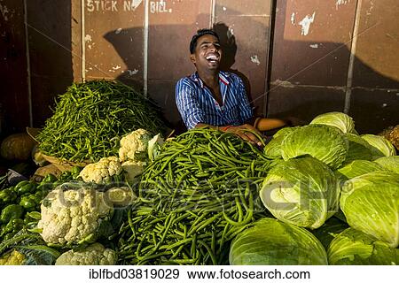 Stock Photo - "A laughing salesman is selling cauliflower, beans and cabbage at an open air vegetable market, Mumbai, Maharashtra, India, Asia". Fotosearch