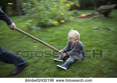 A little boy sitting on a shovel is dragged by an adult across the garden View Large Photo Image Stock Photo - A little boy sitting on a shovel is dragged by an adult across the garden. Fotosearch