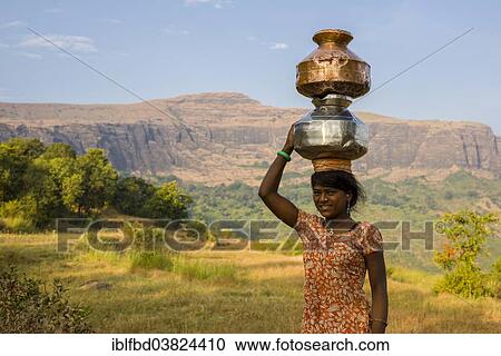 Stock Image - "A local girl is carrying two pots filled with water on her head, Trimbak, Maharashtra, India, Asia". Fotosearch