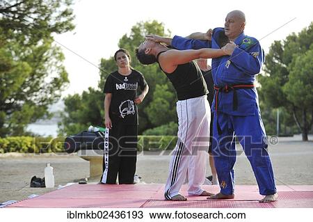 Stock Image - "A martial arts instructor is demonstrating a defensive move on a student in a park, man and woman watching". Fotosearch